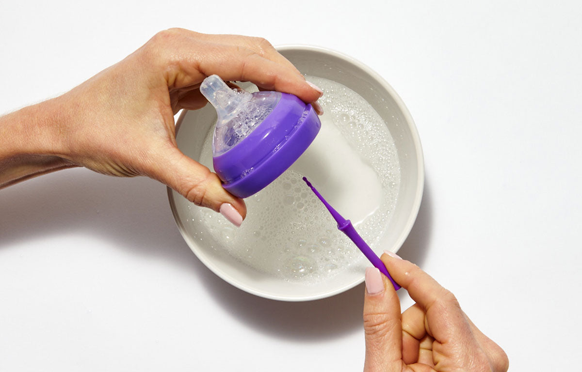 mōmi bottle being washed in a bowl of soapy water and cleaning tool